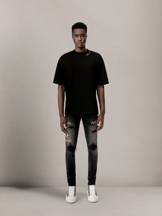 Black crew neck t-shirt with script text detail at neckline, worn with distressed dark jeans.