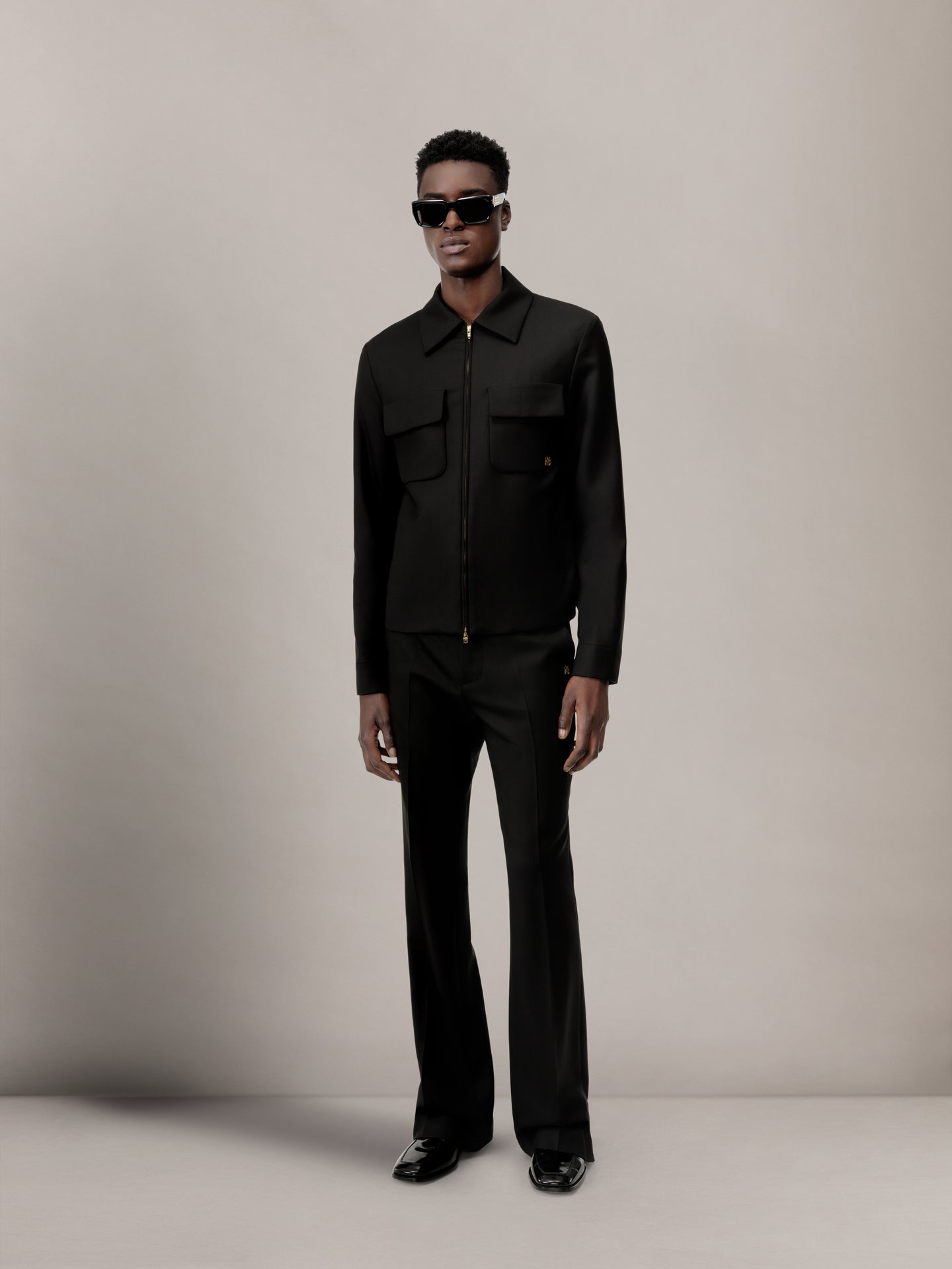 Black blouson jacket with collar and front zip fastening, worn with matching black pants.